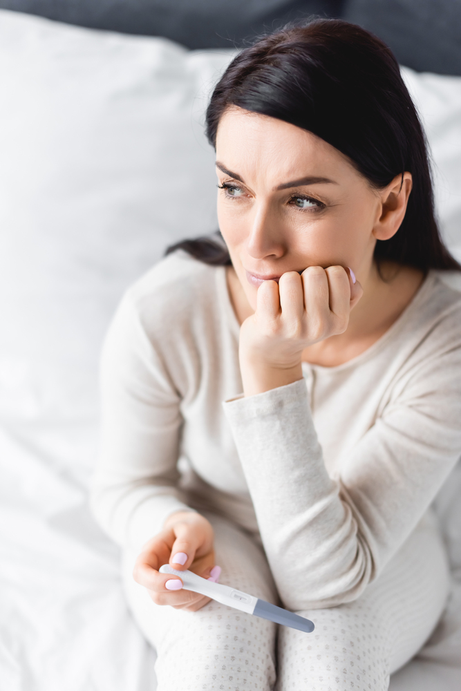 Sad woman holding pregnancy test with negative result